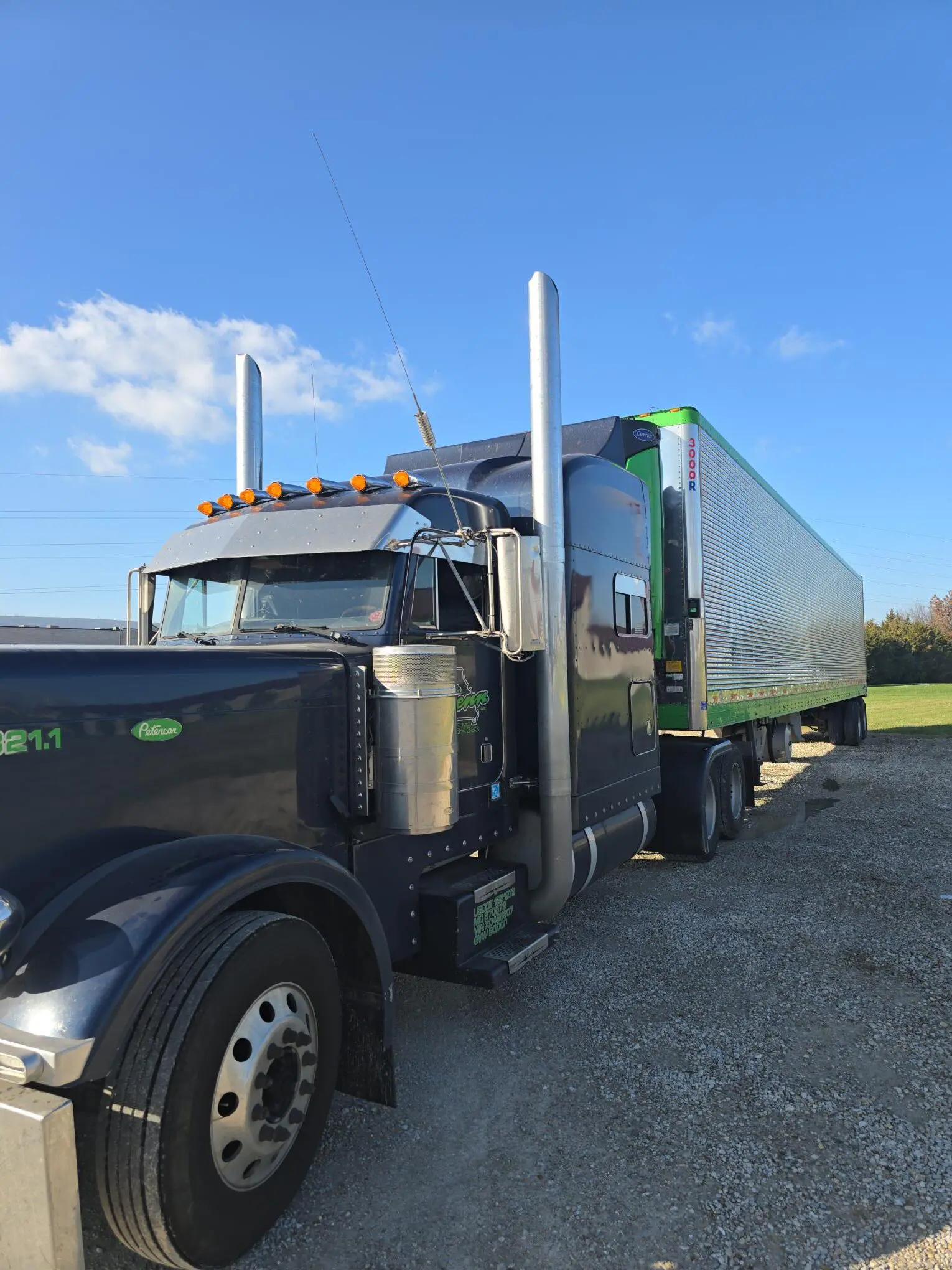 Black semi-truck parked on gravel road.